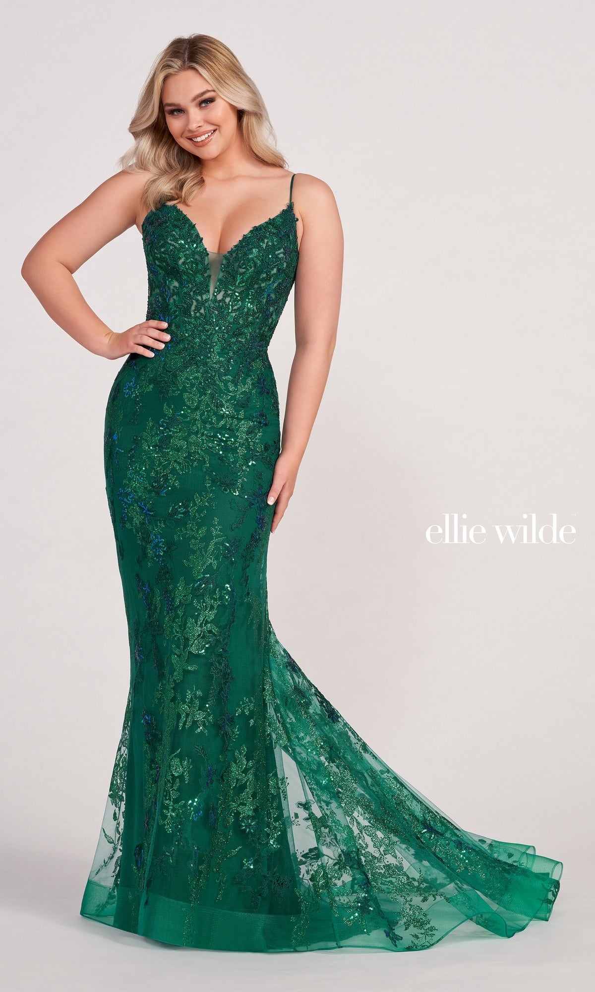 A woman poses in the Embroidered-Lace Ellie Wilde Prom Dress EW34061, a deep green, floor-length mermaid gown with thin straps, a fitted bodice, and delicate floral lace embroidery.
